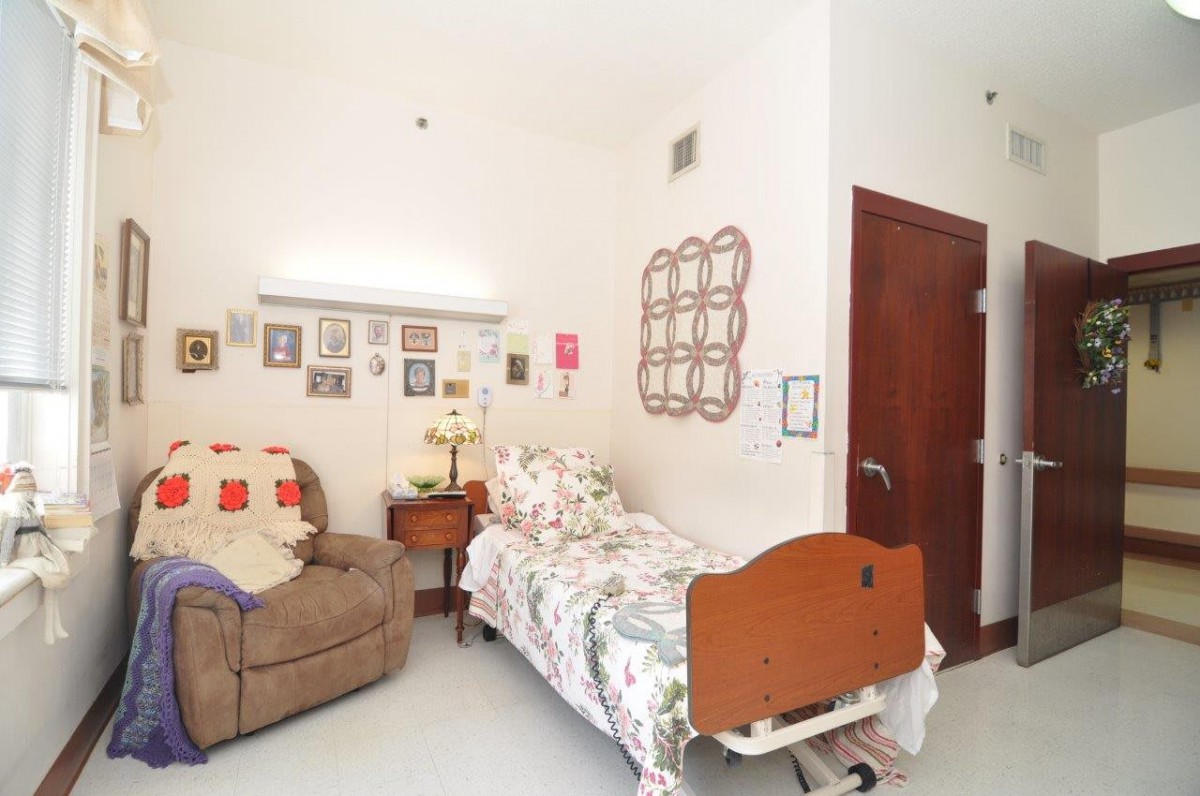 A cozy bedroom with a single bed adorned in floral bedding, an armchair, and various wall decorations.