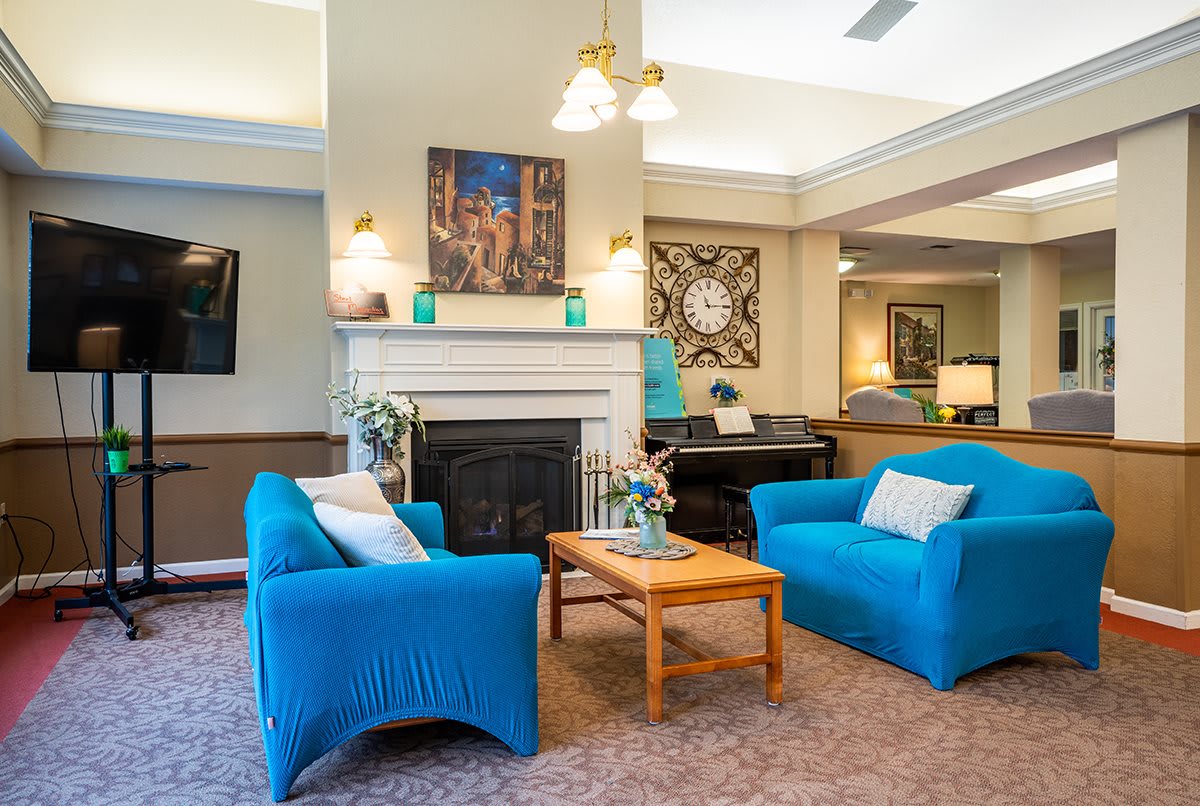 A cozy living room with blue armchairs and a fireplace, featuring a wooden coffee table and elegant decor.