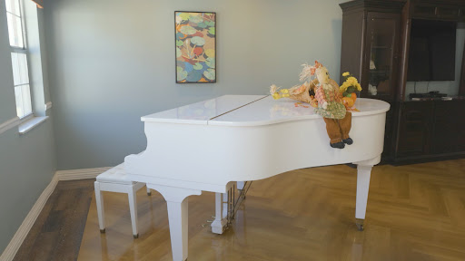 A stylish white grand piano elegantly placed in a cozy living room setting, adorned with a playful figure and colorful artwork.