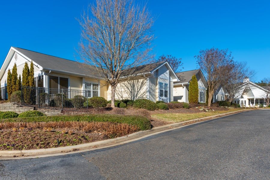 A suburban residential home with a tree and manicured landscape under a clear blue sky.