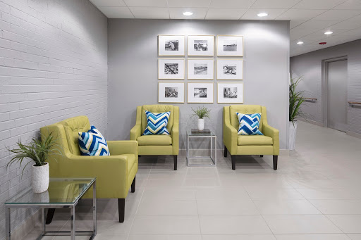 A modern waiting area featuring cozy yellow chairs with geometric patterned pillows, minimalistic dcor, and framed photographs on the wall.