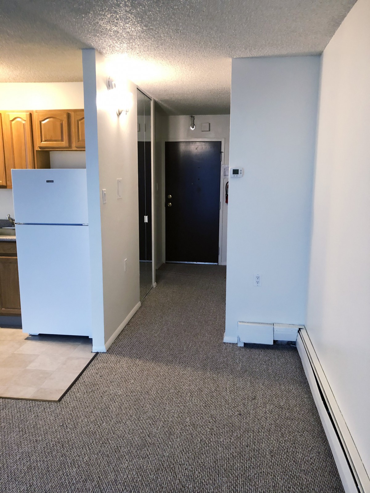 An interior view of a small apartment kitchen and hallway leading to the main door.