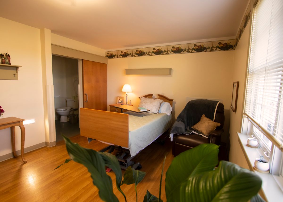A cozy hospital room with a bed, chair, and plants.