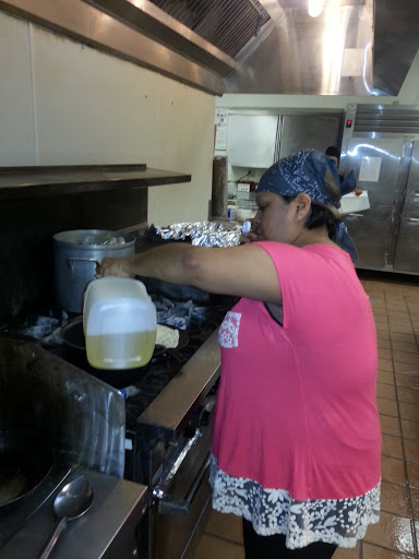 A chef pouring oil into a pot while preparing food in a restaurant kitchen.