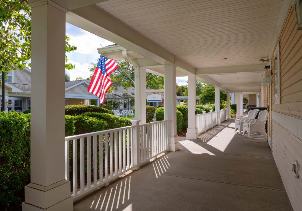 A sunny, peaceful porch featuring an American flag and white railing.