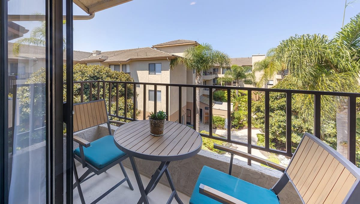 A balcony with a small table and chairs, overlooking an apartment complex on a sunny day.