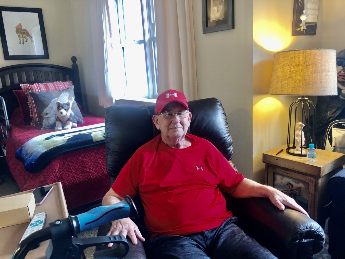 A man wearing a red shirt and hat sits comfortably in a chair inside a cozy room.