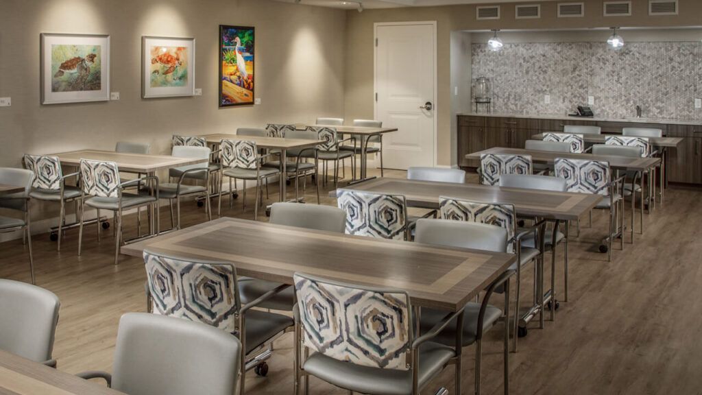 A well-lit conference room with tables and patterned chairs, adorned with colorful artwork on the walls.