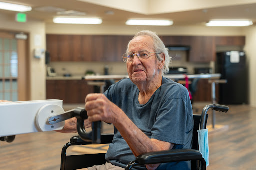 An elderly man sitting in a wheelchair, smiling and enjoying his time in a care facility.