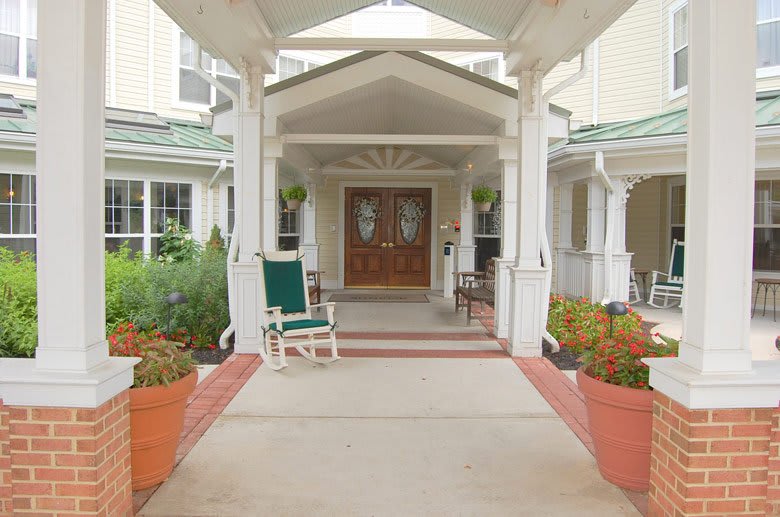 A welcoming entrance to a building with decorative plants and seating on the porch.
