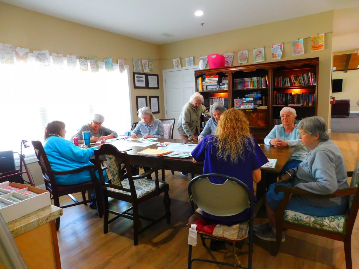 A group of seniors gathered around a table for a meeting in a room with a bookshelf.