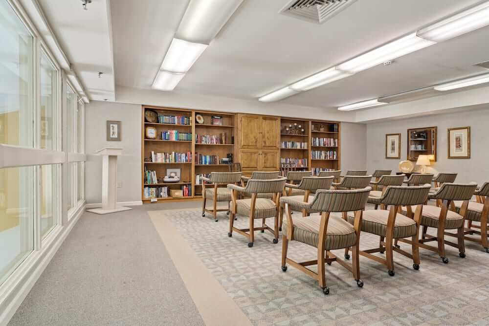 A quiet library setting with rows of chairs facing bookshelves filled with various books.