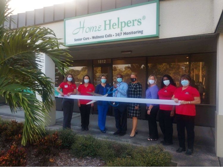 A group of people participate in a ribbon-cutting ceremony outside Home Helpers.