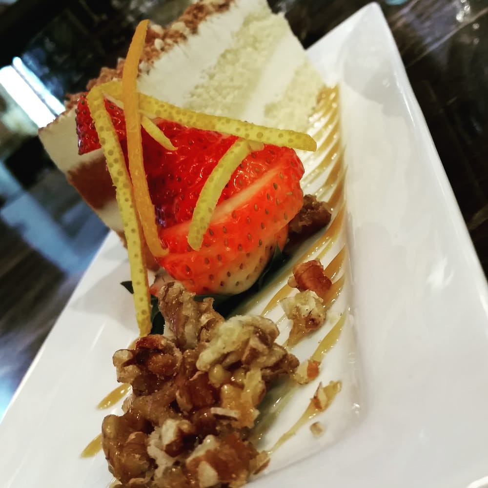 A beautifully plated slice of strawberry cake garnished with nuts and drizzled with sauce.