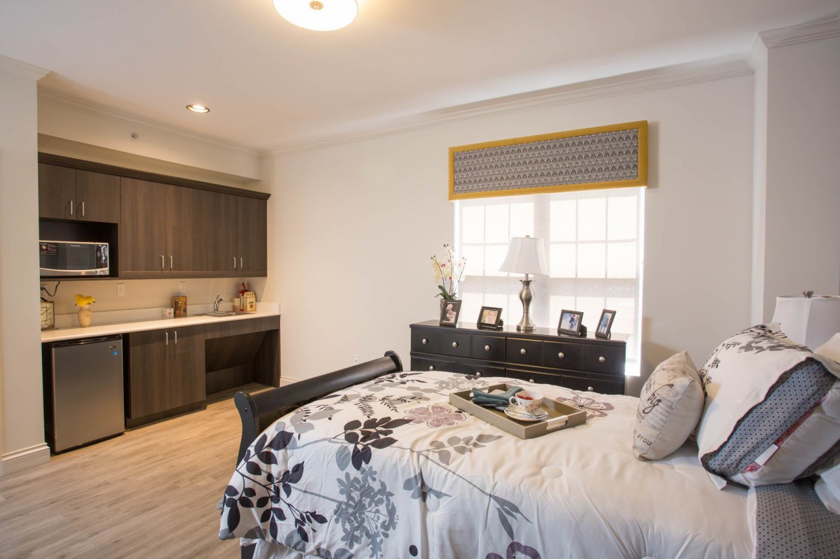 A cozy bedroom featuring a large bed with floral bedding, a dresser with decorative items, and built-in cabinetry.