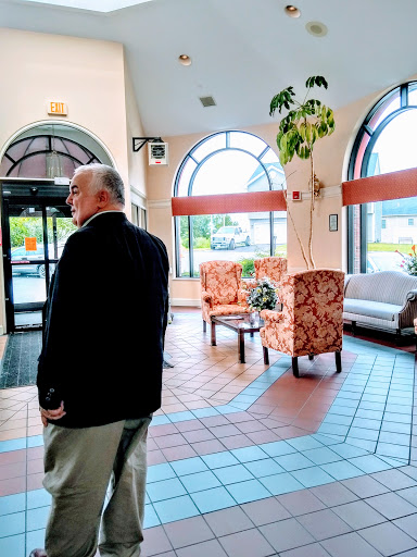 A man stands in a welcoming lobby space, featuring comfortable seating and large windows that allow natural light to fill the room.