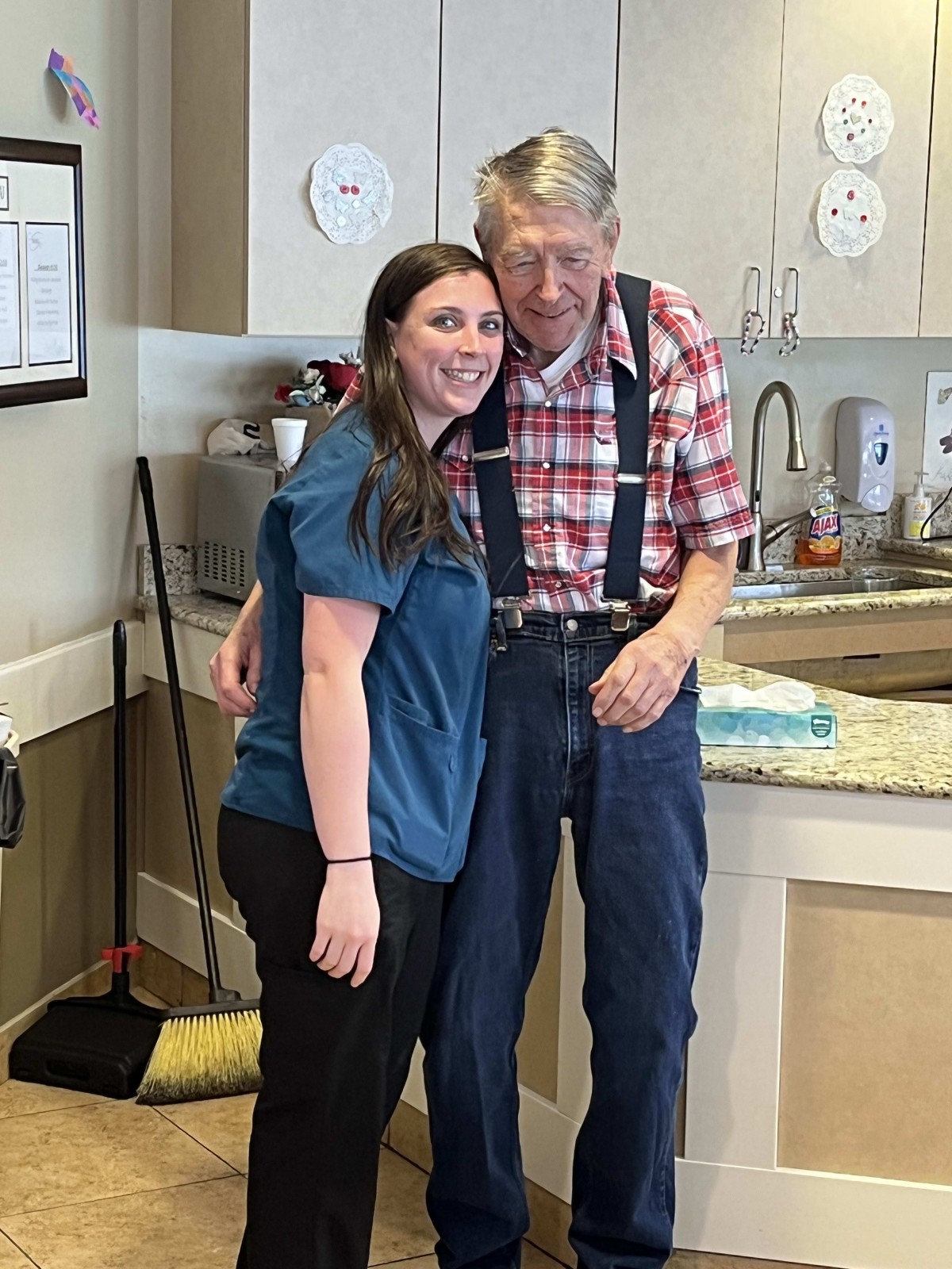 A young woman and an elderly man smiling together in a kitchen setting.