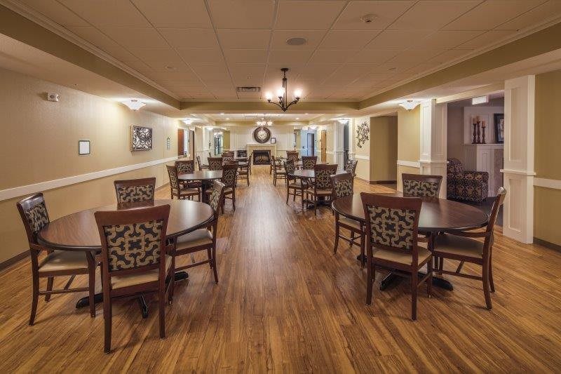 An elegant dining room with wooden flooring and neatly arranged tables and chairs.
