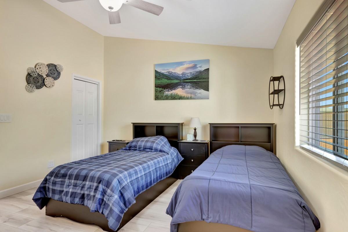A cozy bedroom with two twin beds, featuring matching headboards and bed linens, a nightstand with a lamp in between the beds, and wall art hanging above.
