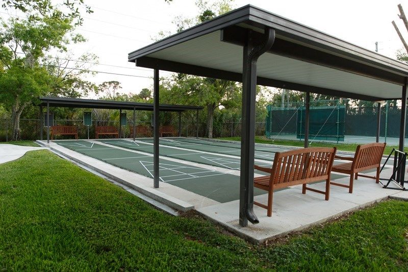An outdoor shuffleboard court with a covered seating area and surrounding greenery.