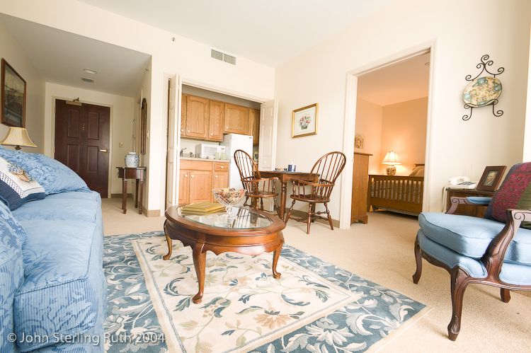 A cozy living room with a coffee table and rug, adjacent to a dining area and kitchenette in an apartment.