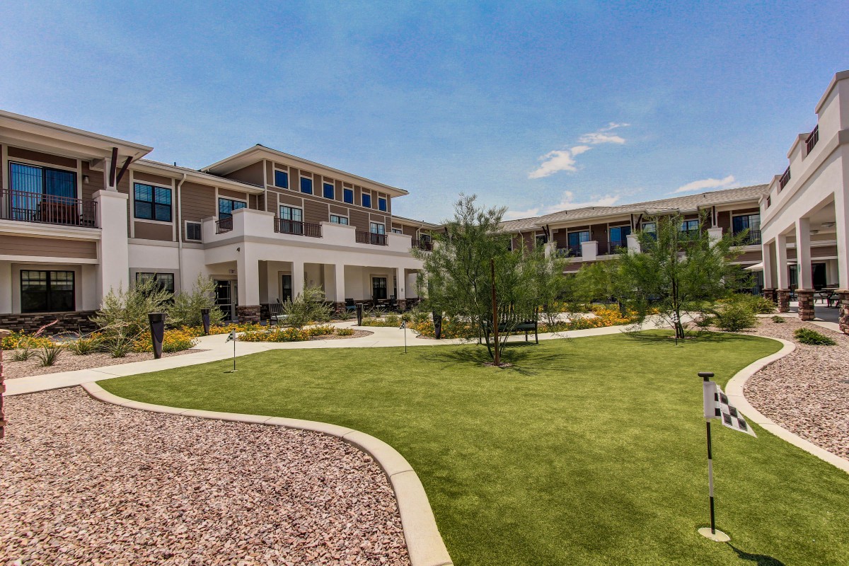 A modern building surrounded by a landscaped garden with grass and trees under a clear blue sky.