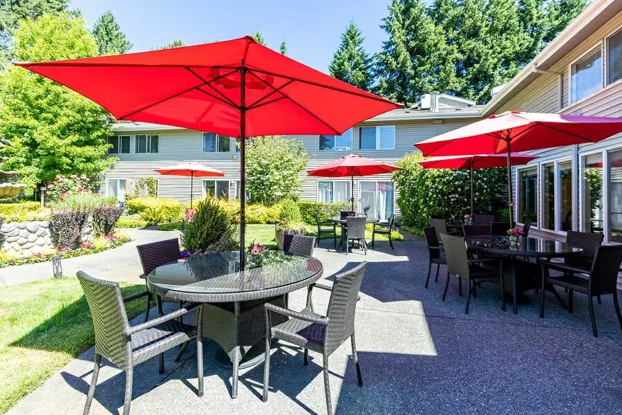 A sunny patio with tables and chairs under vibrant red umbrellas.