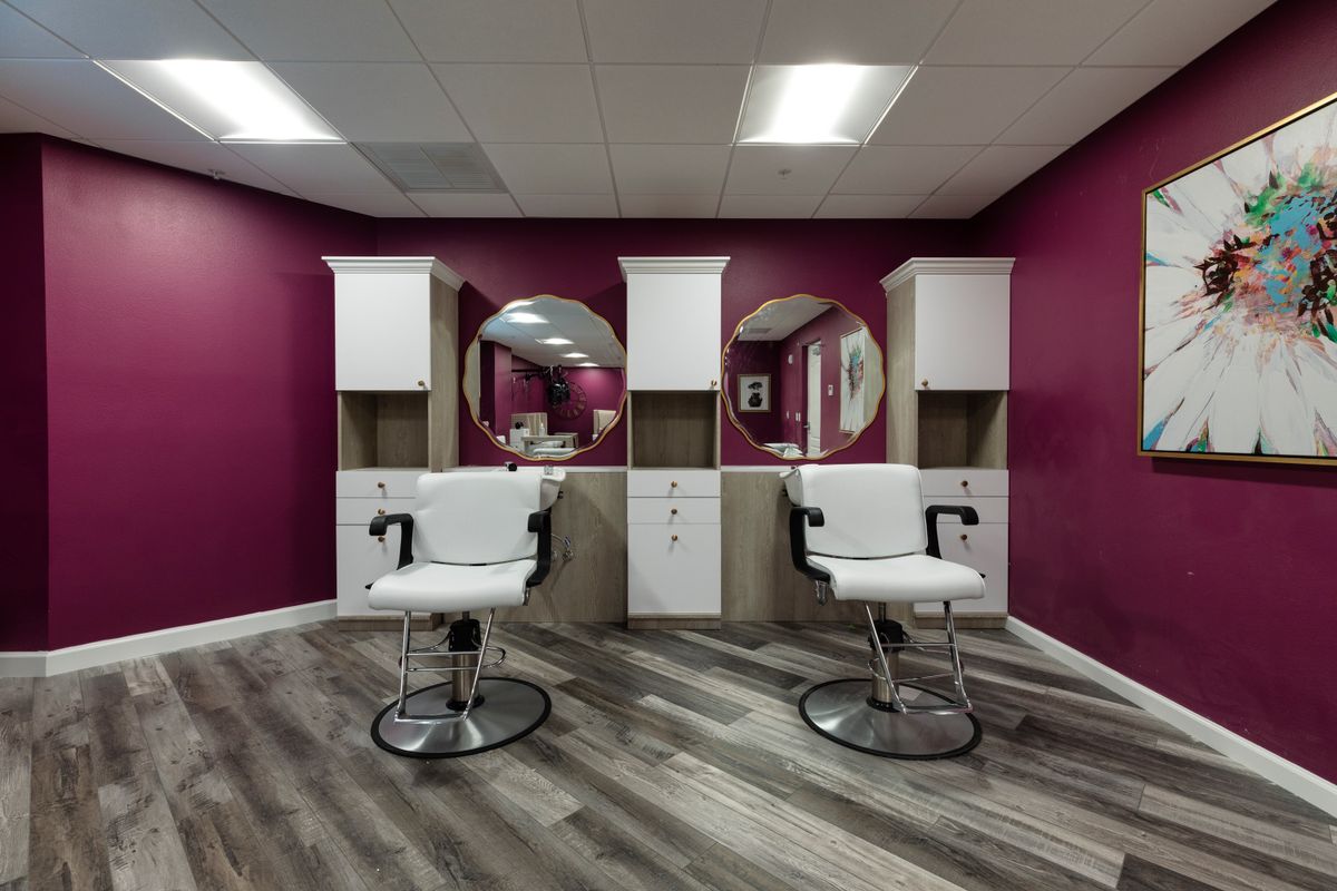 A modern beauty salon with white haircut chairs and large round mirrors against a magenta wall.
