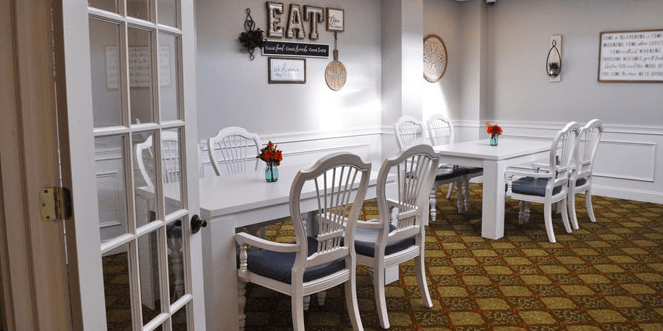 A cozy dining area with white chairs and tables, decorated with flowers and wall art.