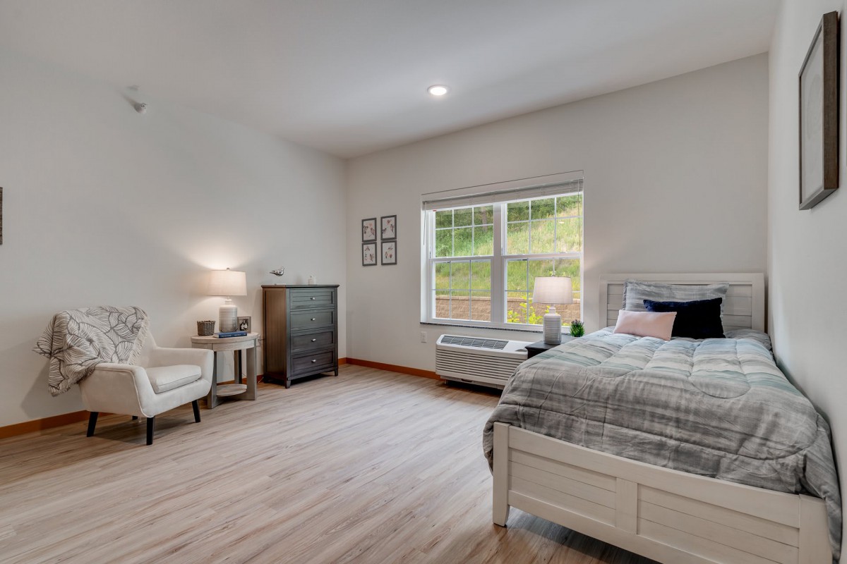 A modern and minimalist bedroom with a bed, chair, and large window.