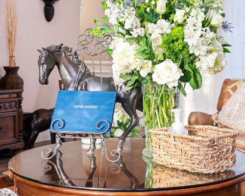 A decorative setup on a table featuring a horse statue, a vase of flowers, and a wicker basket.