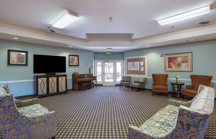A spacious living room with a patterned carpet, sofas, and a piano.