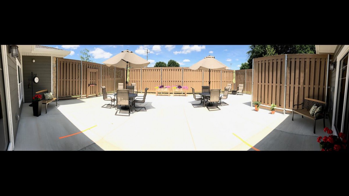 A sunny outdoor patio area with tables, chairs, and umbrellas surrounded by a wooden fence.
