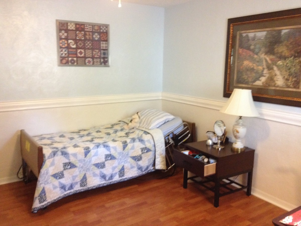 A cozy bedroom with a single bed, adorned with a decorative quilt and accompanied by a nightstand holding a lamp and an alarm clock.