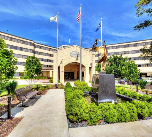 A well-maintained courtyard featuring an entrance flanked by flags and a statue, surrounded by greenery.