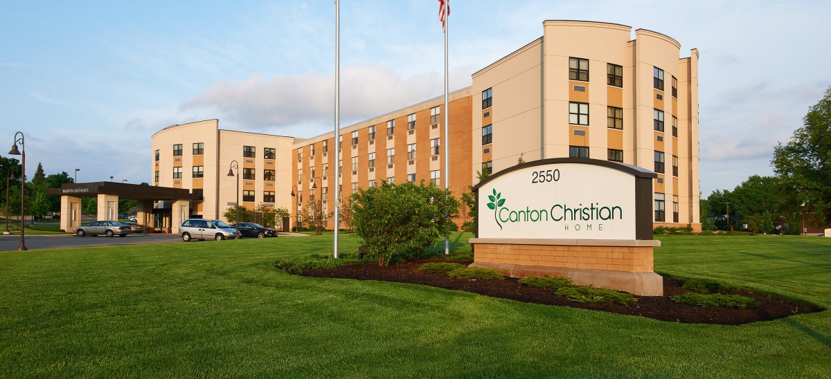 A large brick building with a sign in front, surrounded by grass and flags.