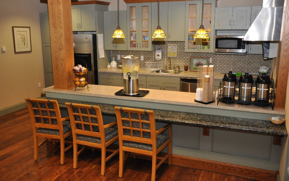 A modern kitchen with a bar counter and three wooden stools, featuring pendant lighting and stainless steel appliances.