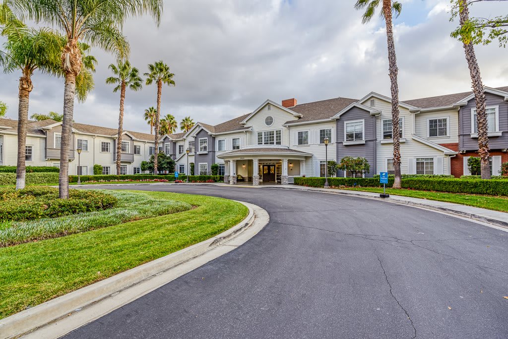 A residential building with a round driveway and palm trees under a cloudy sky.