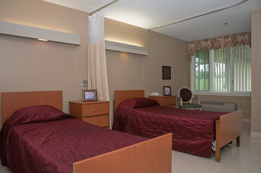 A cozy and well-lit bedroom featuring twin beds with burgundy covers, accented by wooden furniture and a view outside.