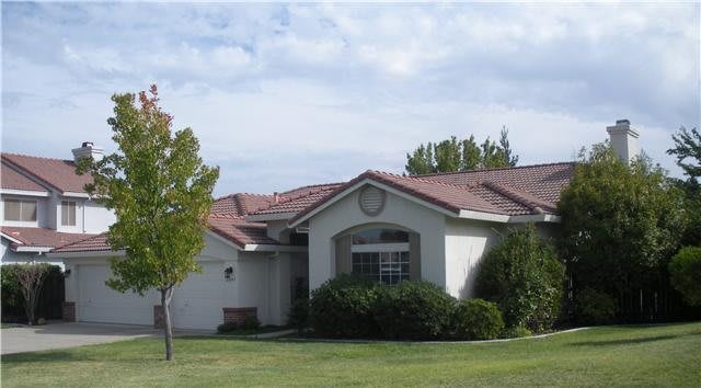 A suburban house with a well-maintained lawn and surrounding trees under a partly cloudy sky.