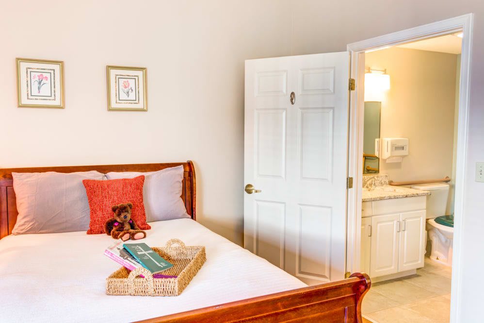 A cozy bedroom with a neatly made bed, featuring pillows and a tray, adjacent to an open door leading to a bathroom.