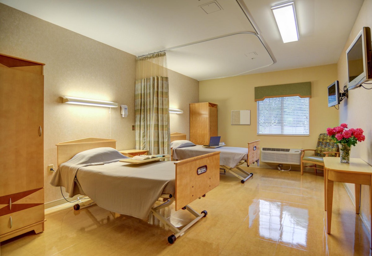 A hospital room with two beds, medical equipment, and a window.