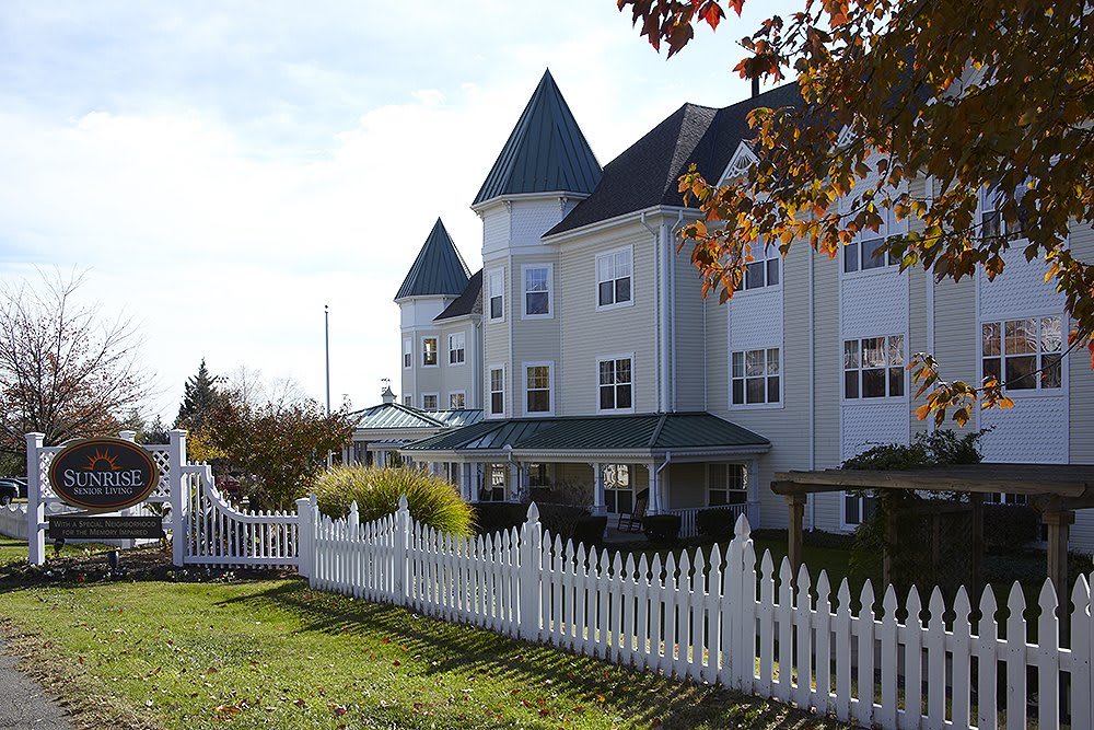 A white residential building with a pointed roof and a surrounding picket fence.