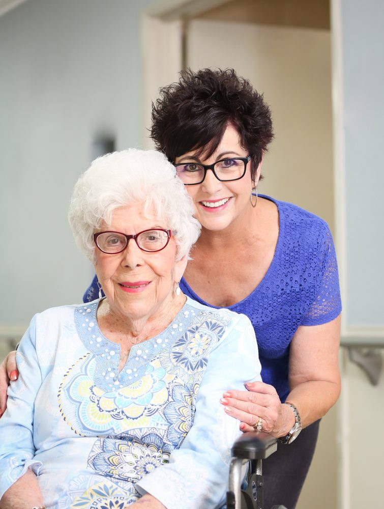 A smiling elderly woman and a younger woman posing together indoors.
