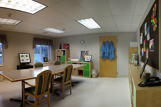 A well-lit office space featuring a meeting table surrounded by chairs, a desk area with shelves, and a door leading to another room.