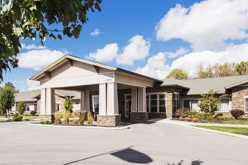 An exterior view of a modern building with a driveway and landscaped surroundings under a partly cloudy sky.