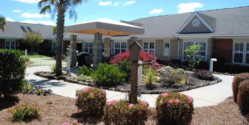 A well-maintained residential building with colorful gardens under a clear blue sky.