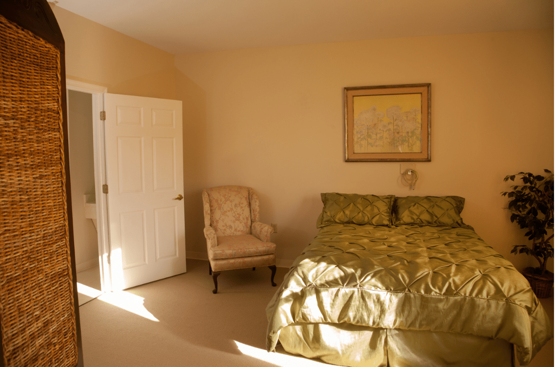 A cozy bedroom with a green bedspread, a chair, and a painting on the wall.