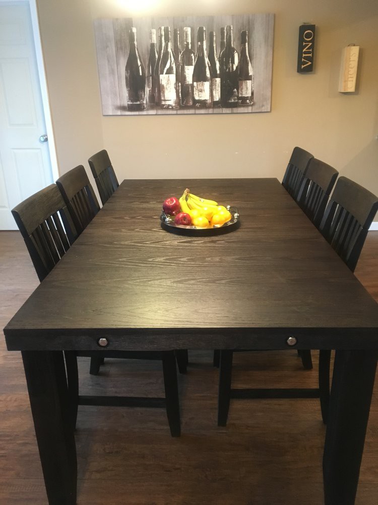 A dining room setup with a dark wooden table, surrounded by chairs and a fruit bowl centerpiece.