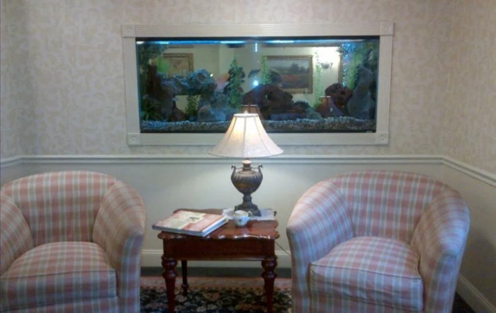 A cozy waiting area with an aquarium, two chairs, and a lamp on a wooden table.